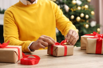 Photo of Man decorating Christmas gift box at wooden table indoors, closeup