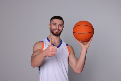 Photo of Athletic young man with basketball ball showing thumb up on light grey background
