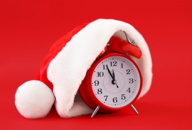 Photo of Alarm clock with Santa hat on red background. New Year countdown