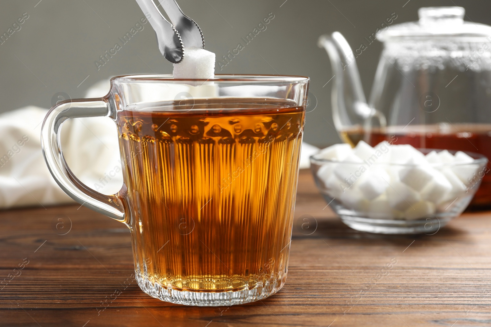 Photo of Adding sugar cube into cup of tea at wooden table, closeup