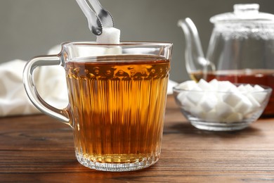 Adding sugar cube into cup of tea at wooden table, closeup