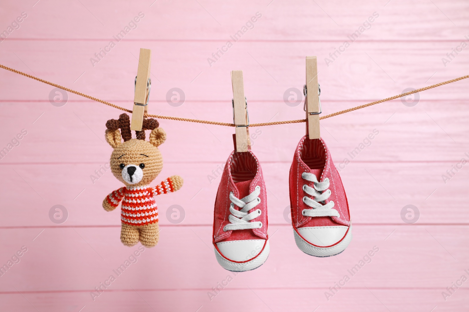 Photo of Cute baby sneakers and crochet toy drying on washing line against pink wooden wall