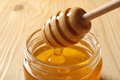 Photo of Pouring honey from dipper into jar on wooden table, closeup