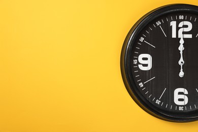 Modern black clock on yellow background, top view. Space for text