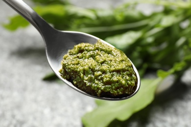 Spoon of tasty arugula pesto on blurred background, closeup