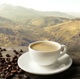 Cup of aromatic hot coffee on wooden table and beautiful view of mountain landscape