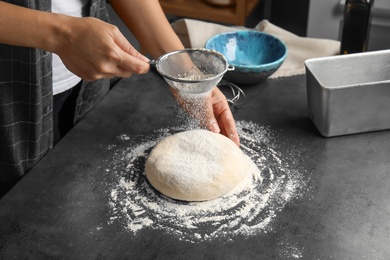 Photo of Woman sprinkling dough for pastry with flour on table