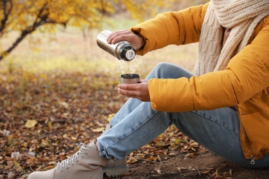 Woman with thermos sitting on ground outdoors, closeup