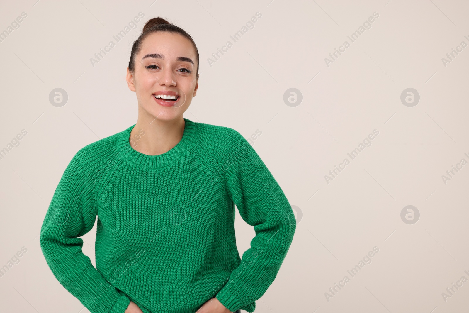 Photo of Beautiful young woman in stylish warm sweater on light grey background, space for text