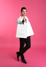 Young handsome man holding white paper bags on pink background. Mockup for design