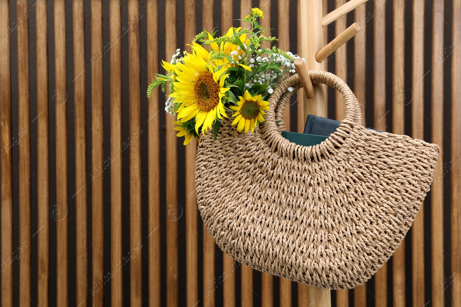 Photo of Stylish beach bag with beautiful bouquet of wildflowers and books hanging on coat stand against wood slat wall. Space for text