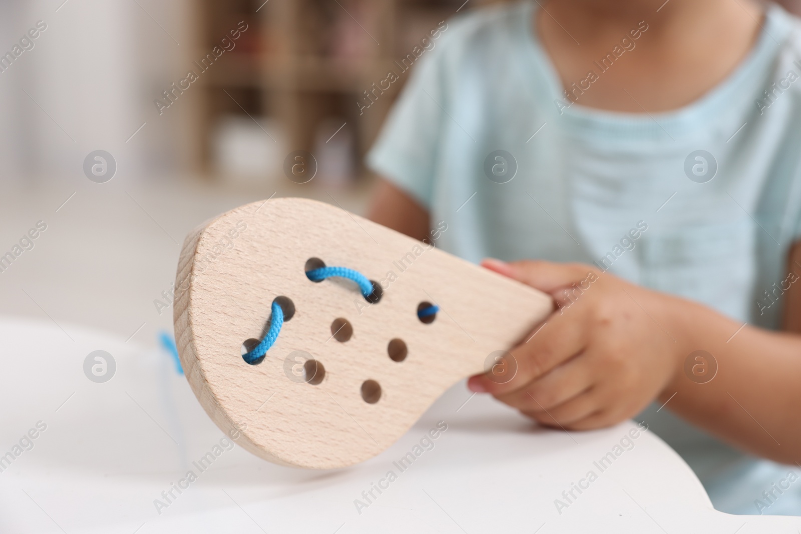 Photo of Motor skills development. Little girl playing with wooden lacing toy at table indoors, closeup