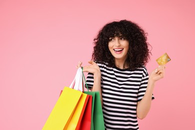 Photo of Happy young woman with shopping bags and credit card on pink background