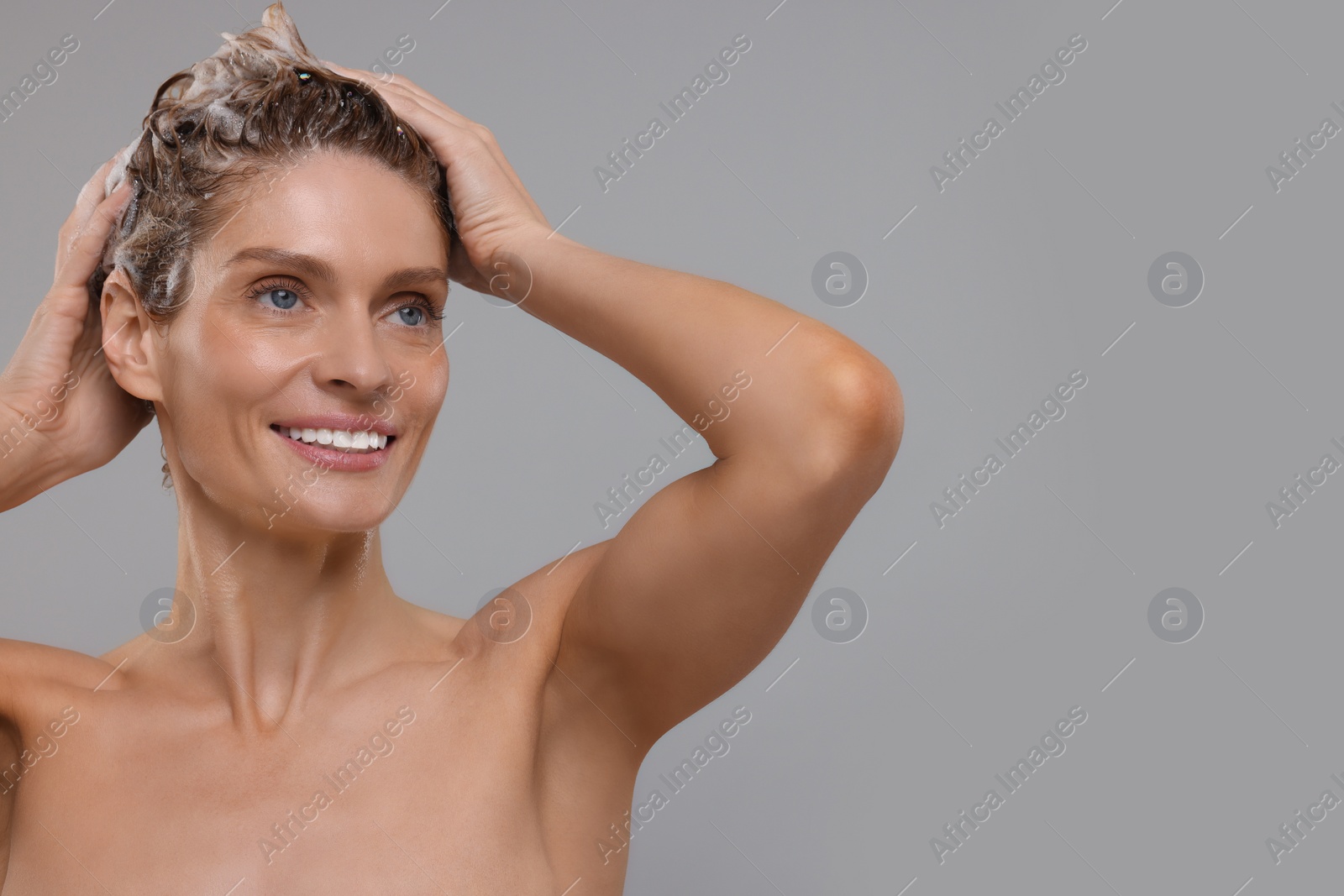 Photo of Beautiful happy woman washing hair on light grey background. Space for text