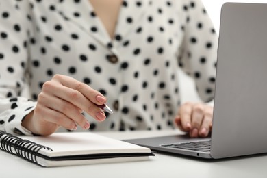 Photo of E-learning. Woman taking notes during online lesson at table indoors, closeup