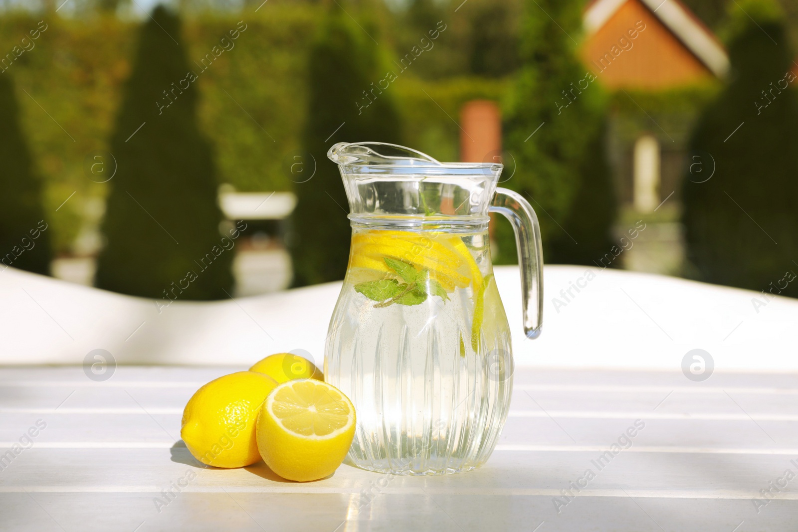 Photo of Jug of water with lemons and mint on white wooden table outdoors