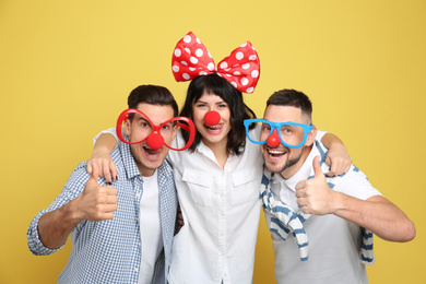 Group of friends with funny accessories on yellow background. April fool's day