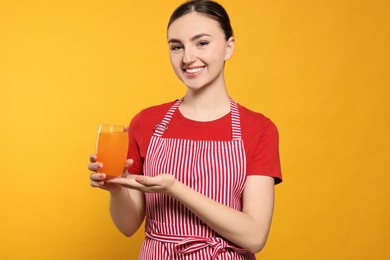 Photo of Beautiful young woman in clean striped apron with glass of juice on orange background