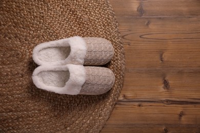 Pair of warm stylish slippers and wicker mat on wooden floor, flat lay. Space for text