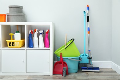 Photo of Shelving unit with detergents and cleaning tools near light grey wall indoors