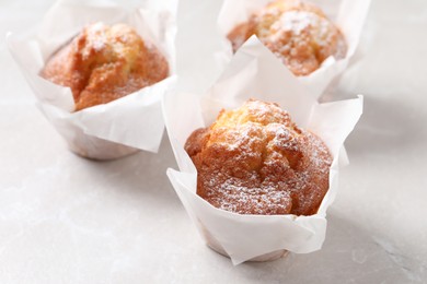 Photo of Delicious muffins with powdered sugar on light table, closeup