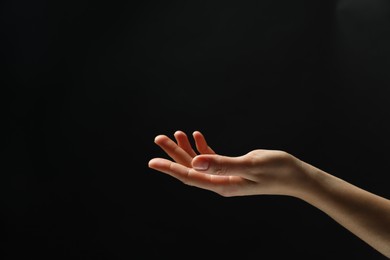 Woman holding something in hand on black background, closeup. Space for text