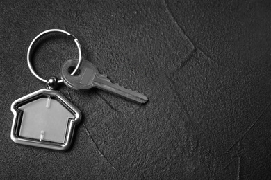 Photo of Key with trinket in shape of house on black stone background, top view and space for text. Real estate agent services