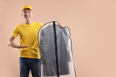 Dry-cleaning delivery. Happy courier holding garment cover with clothes on beige background, space for text