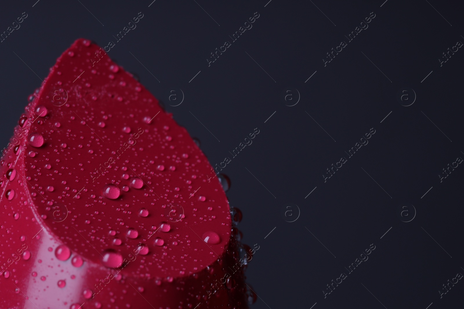 Photo of Red lipstick with water drops on dark gray background, macro view. Space for text