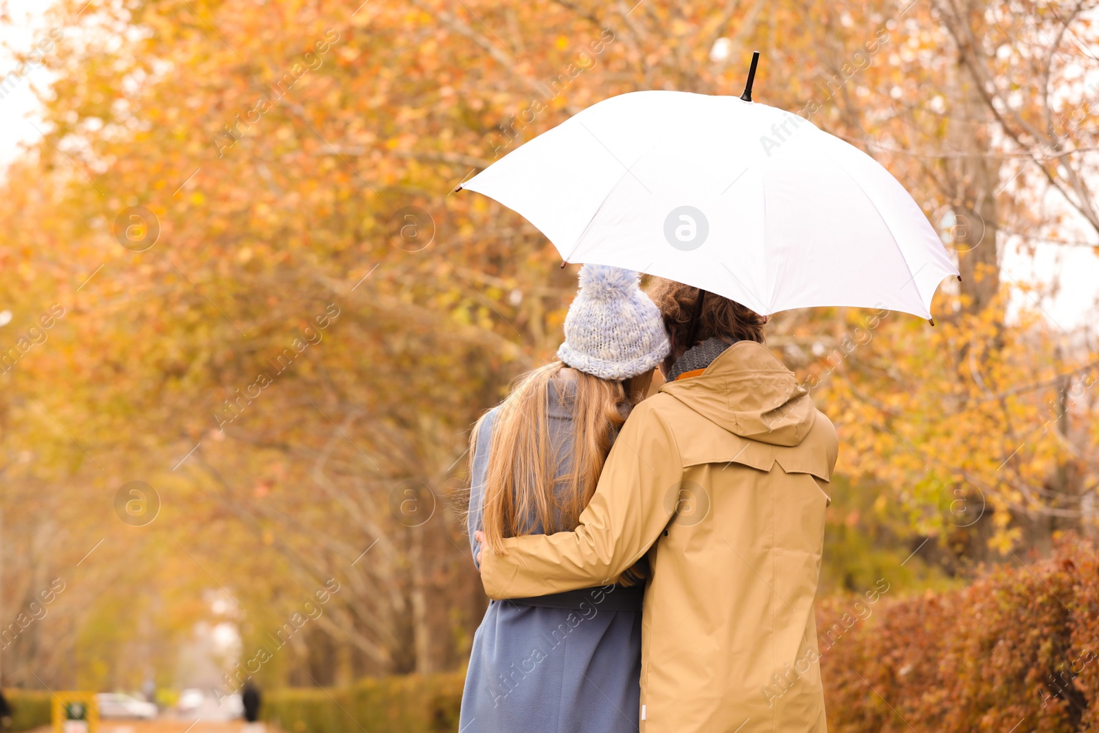 Photo of Young romantic couple with umbrella in park on autumn day