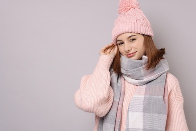 Photo of Beautiful woman in warm scarf and hat on gray background, space for text