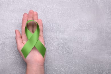 Photo of World Mental Health Day. Woman holding green ribbon on light grey background, top view with space for text