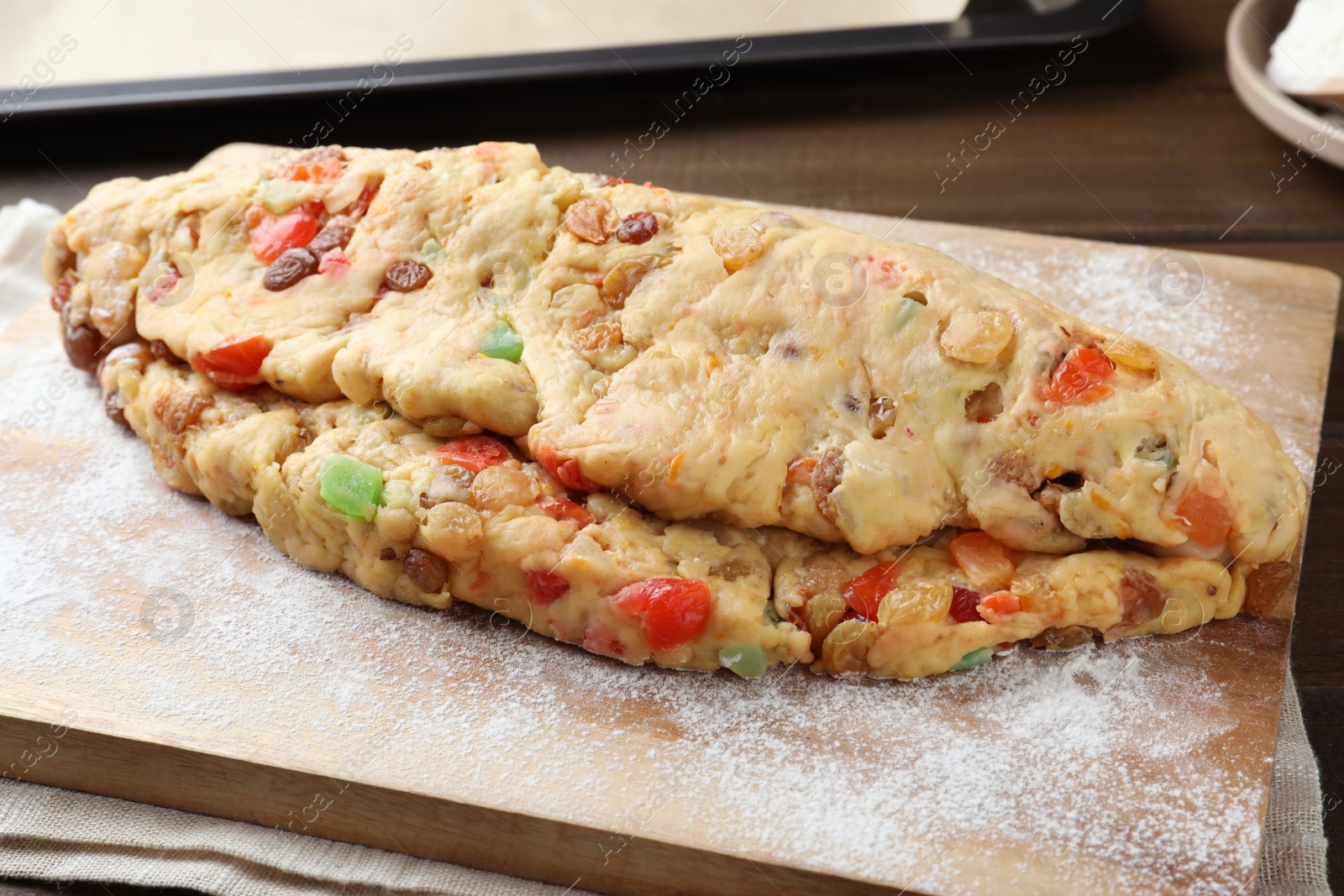 Photo of Unbaked Stollen with candied fruits and raisins on wooden board, closeup