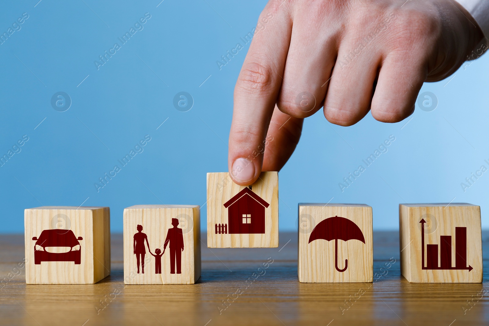 Image of Man arranging cubes with different icons in row on wooden table against light blue background, closeup. Insurance concept