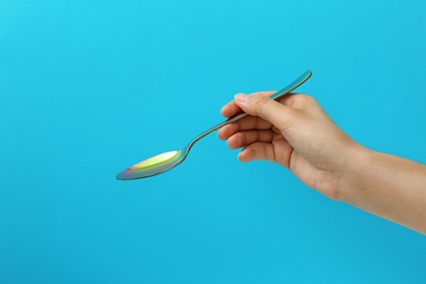 Photo of Woman holding empty table spoon on color background, closeup