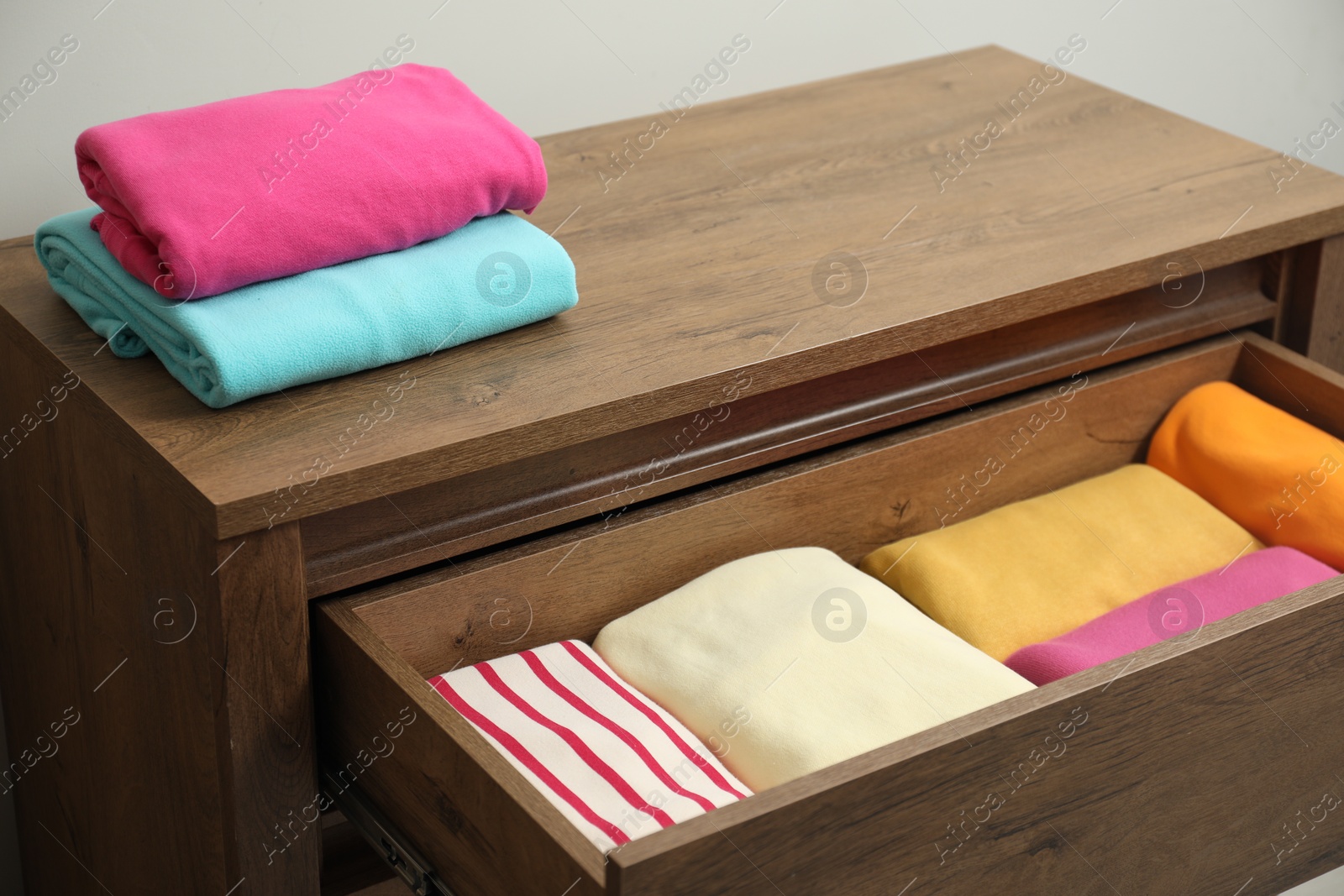 Photo of Wooden chest of drawers with different folded clothes indoors, closeup