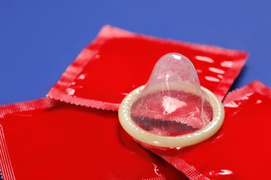 Photo of Unpacked condom and packages on blue background, closeup. Safe sex