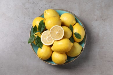 Fresh lemons and green leaves on grey table, top view