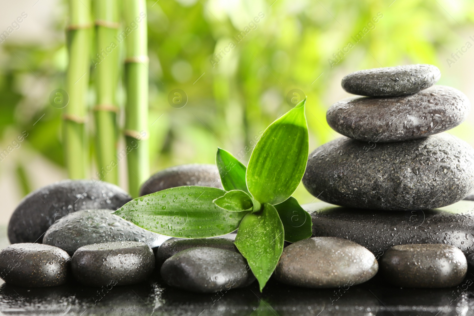 Photo of Bamboo leaves with spa stones on table against blurred background. Space for text