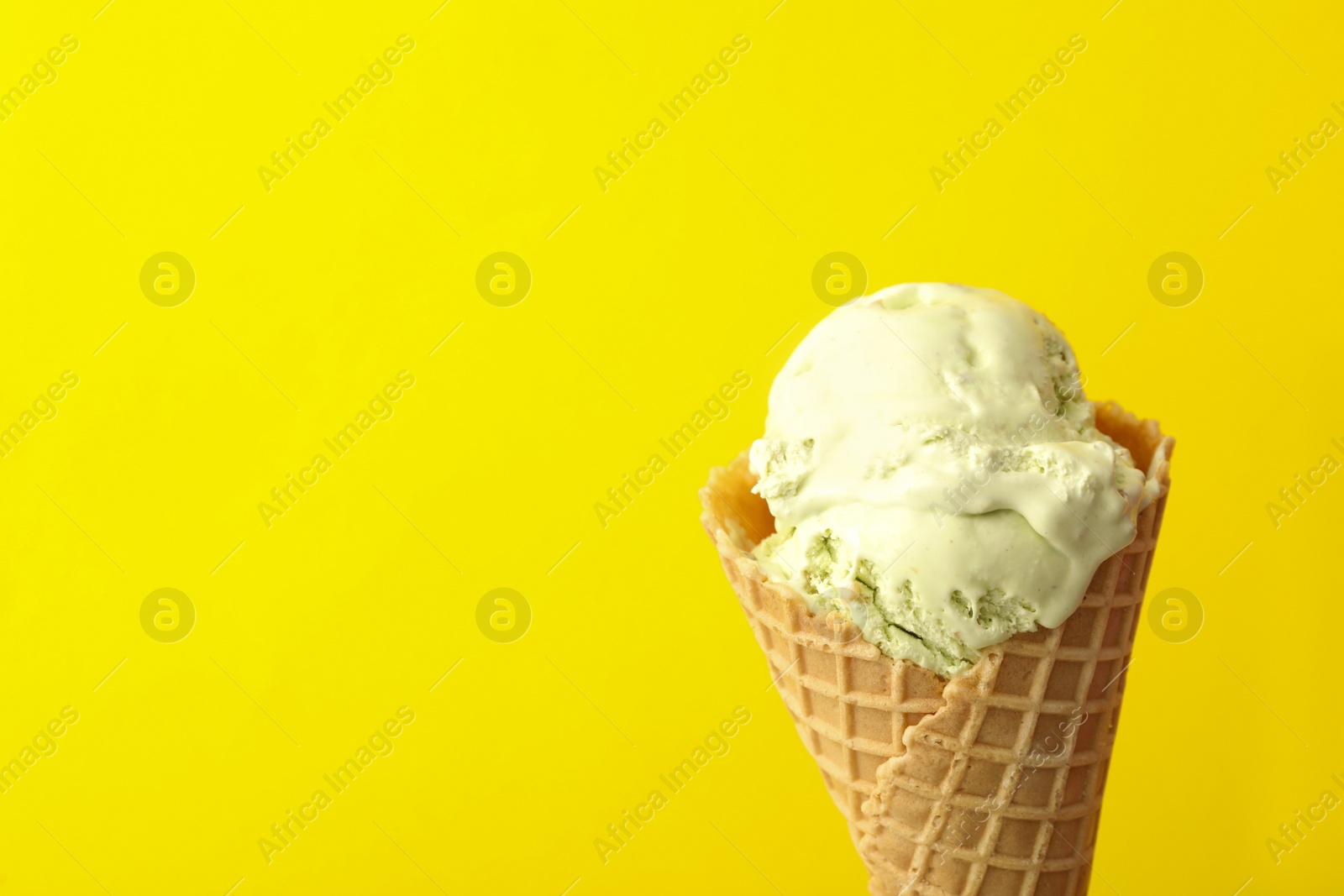 Photo of Delicious ice cream in waffle cone on yellow background, closeup. Space for text