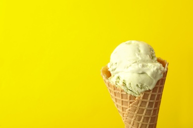 Photo of Delicious ice cream in waffle cone on yellow background, closeup. Space for text