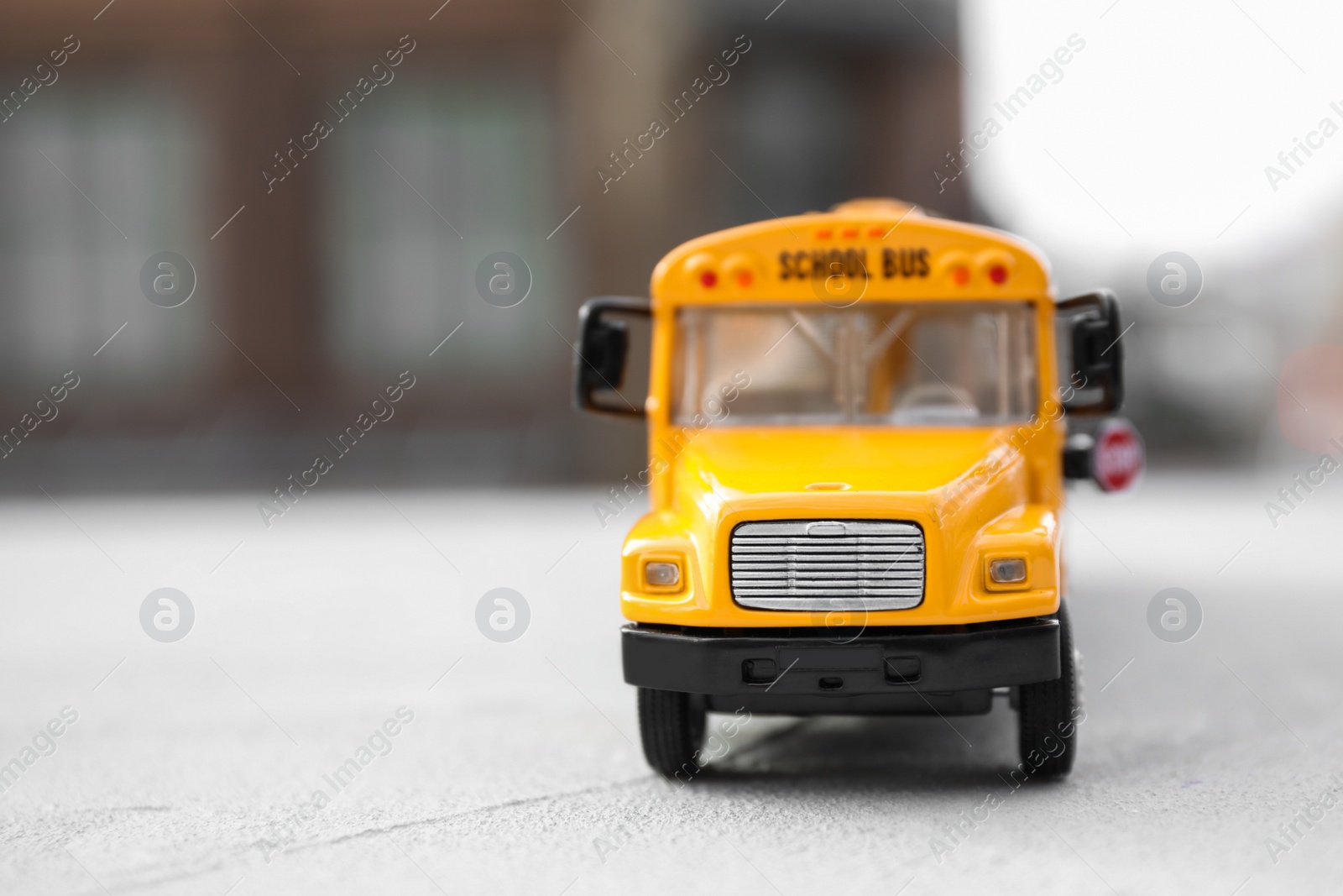 Photo of Yellow toy school bus against blurred background, space for text. Transport for students