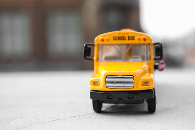 Photo of Yellow toy school bus against blurred background, space for text. Transport for students