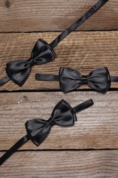 Stylish black bow ties on wooden background, flat lay