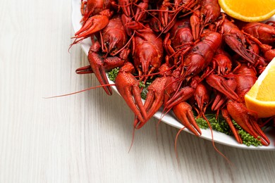 Plate with delicious red boiled crayfish and orange on white wooden table
