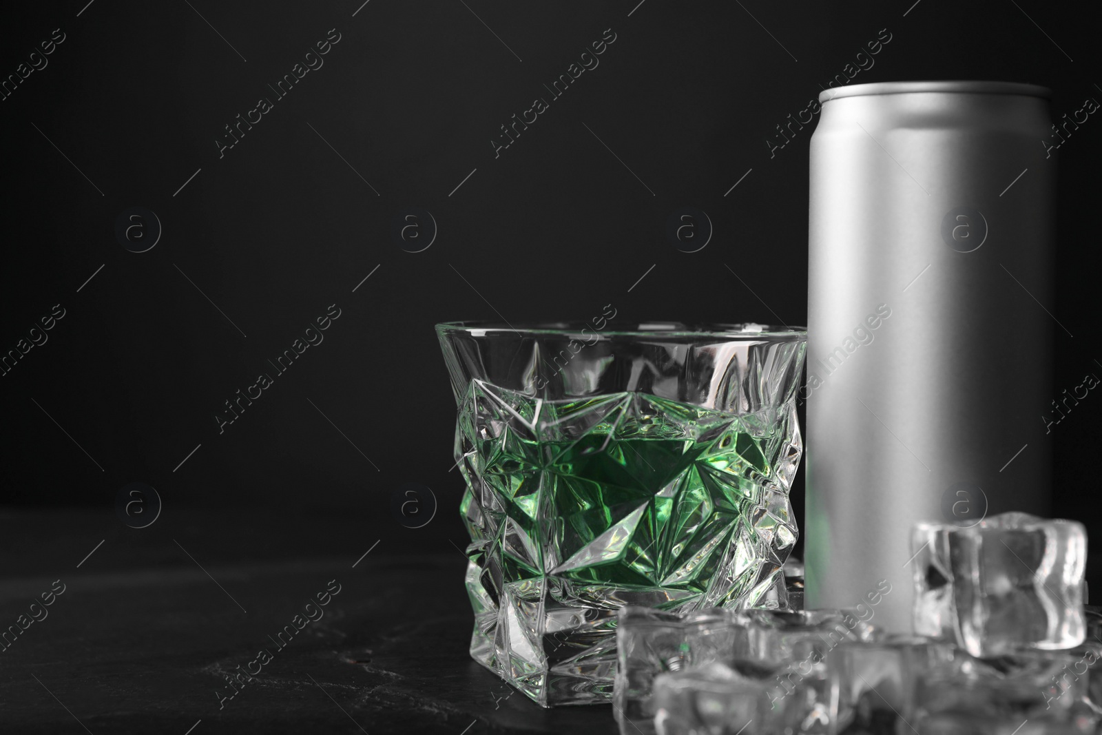 Photo of Energy drink in glass, aluminium can and ice cubes on black table. Space for text