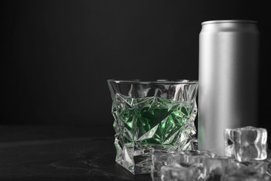 Energy drink in glass, aluminium can and ice cubes on black table. Space for text