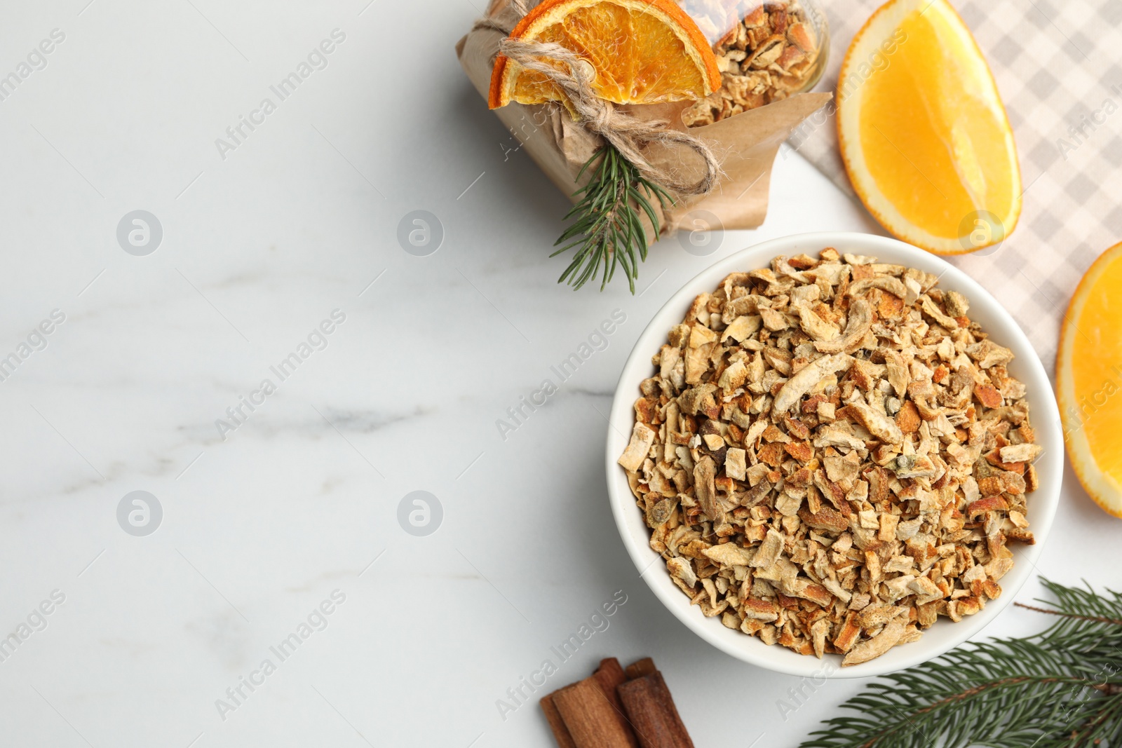 Photo of Bowl of dried orange zest seasoning, fresh fruit and cinnamon on white marble table, flat lay. Space for text