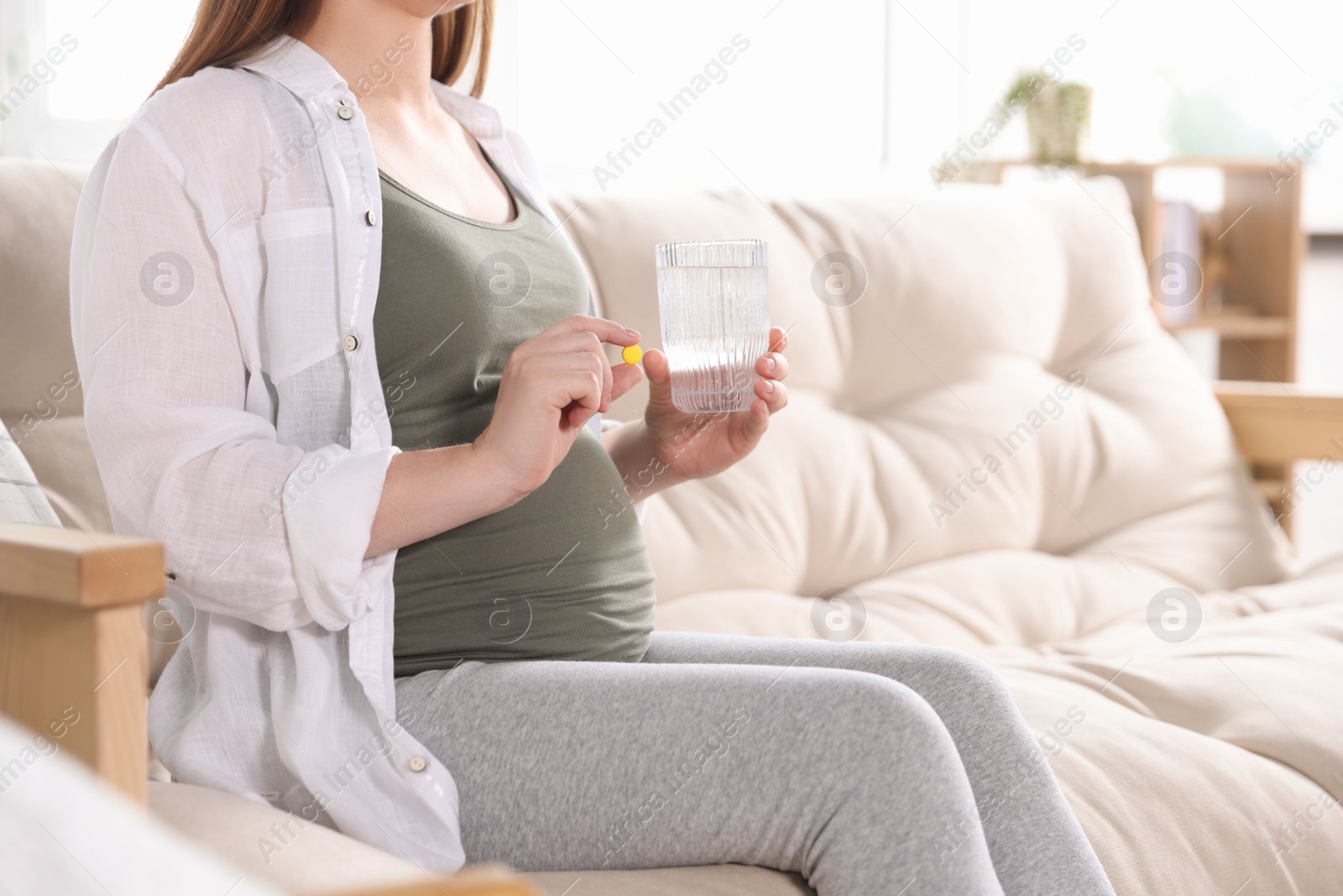 Photo of Pregnant woman holding pill and glass with water at home, closeup