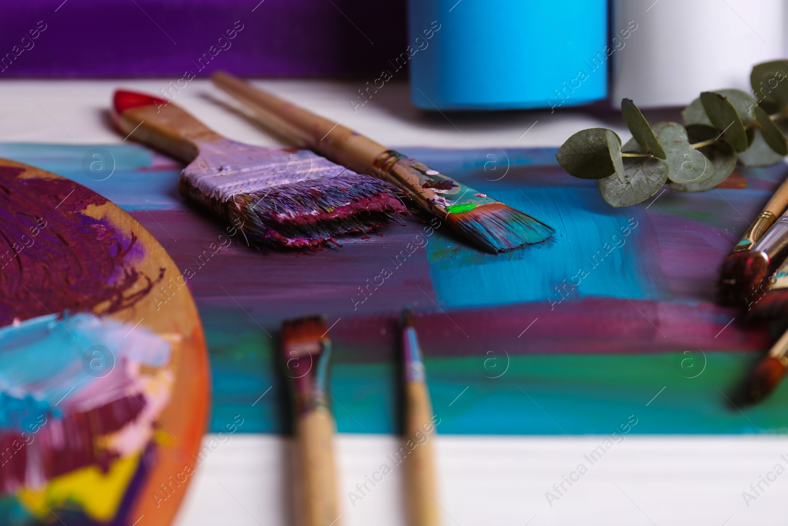 Photo of Colorful paints, wooden artist's palette and different brushes on white table, closeup